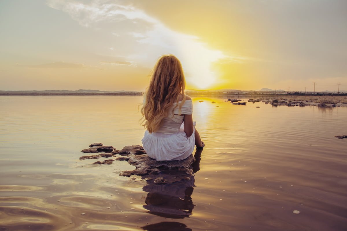 Chica sentada de espaldas en el mar en un atardecer